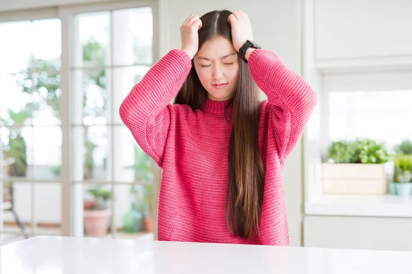 美しいアジアの女性のピンクのセーターを着たので必死と強調した頭痛に苦しんで白いテーブルの痛みと片頭痛 頭に手 — ストック写真
