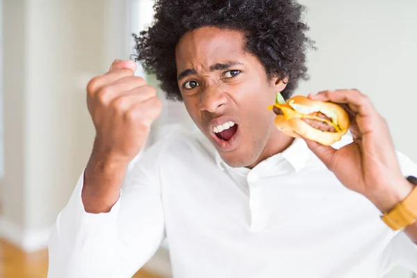 イライラお昼を食べるアフリカ系アメリカ人の飢えた男ハンバーガーとイライラ叫び狂気と上げられた手で 叫んで 怒りと怒りの概念 — ストック写真