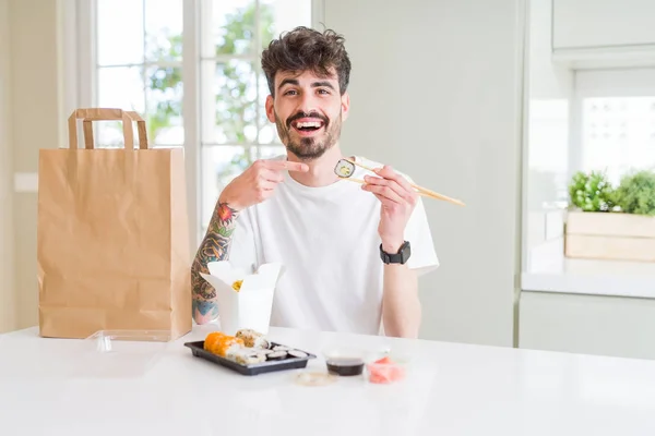 Młody Mężczyzna Jedzenie Sushi Azjatycki Dostawa Domu Bardzo Szczęśliwy Wskazując — Zdjęcie stockowe