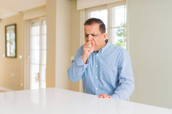 Middle age man sitting at home feeling unwell and coughing as symptom for cold or bronchitis. Healthcare concept.