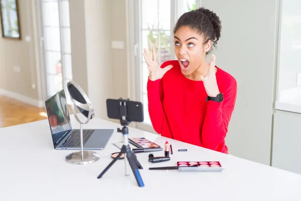 Young african american influencer woman recording make up tutorial crazy and mad shouting and yelling with aggressive expression and arms raised. Frustration concept.