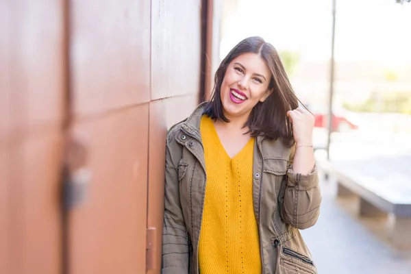 Beautiful young woman smiling confident and cheerful leaning on the wall, walking on the street of the city on a sunny day