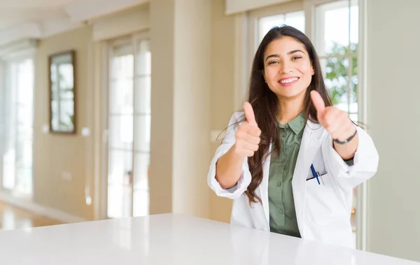 在诊所穿医用外套的年轻女子担任心理医生或医生 批准用手做积极的手势 竖起大拇指微笑 为成功而高兴 看着镜头 赢家的手势 — 图库照片