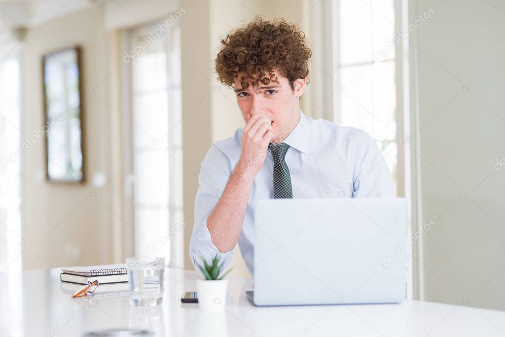 Young business man working with computer laptop at the office smelling something stinky and disgusting, intolerable smell, holding breath with fingers on nose. Bad smells concept.