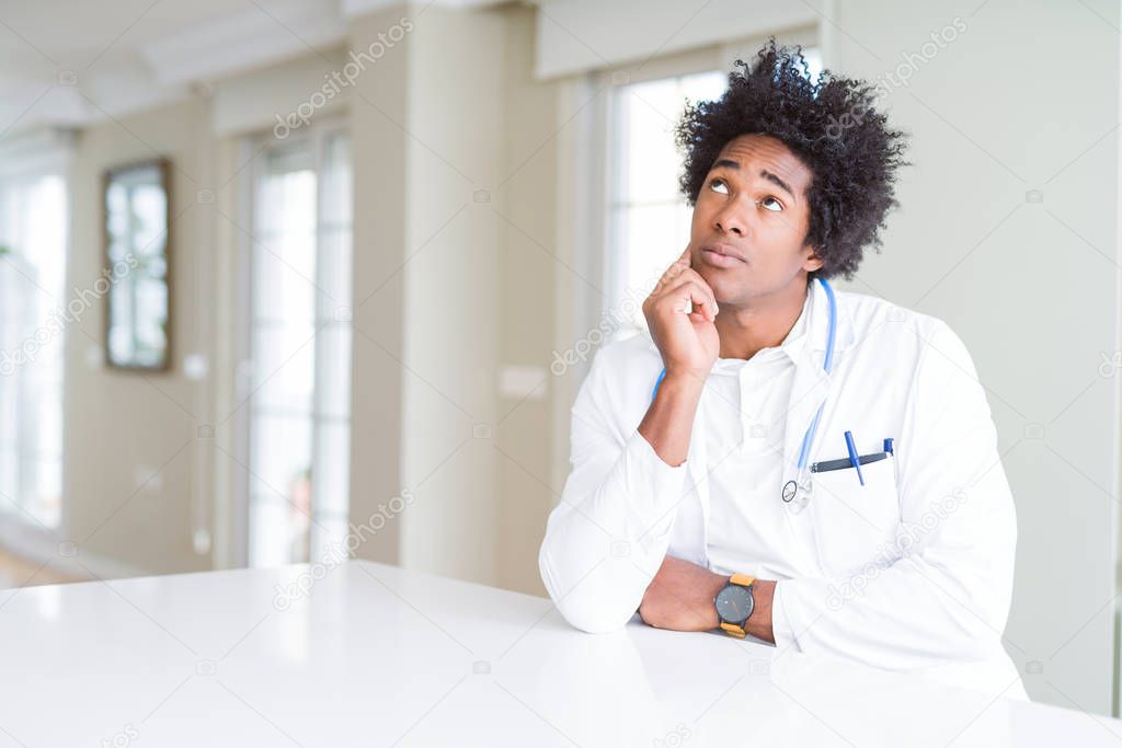 African American doctor man at the clinic with hand on chin thinking about question, pensive expression. Smiling with thoughtful face. Doubt concept.