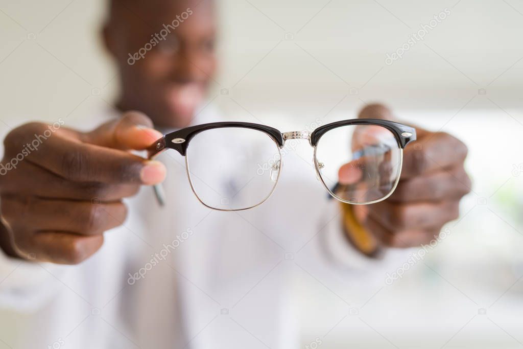 African american optiian man holding and showing glasses lens to custumers at the optics shop while smiling confident