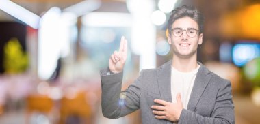 Young business man wearing glasses over isolated background Swearing with hand on chest and fingers, making a loyalty promise oath clipart