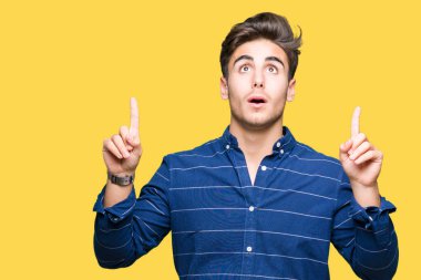 Yakışıklı delikanlı izole arka plan üzerinde Donanma gömlek giymiş hayrete ve yukarıya bakıyor ve parmakları ile işaret ve silah kaldırdı şaşırttı.