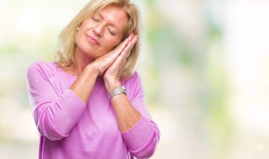 Orta yaş uyku yorgun hayal ve ellerle birlikte poz ile kapalı gözler gülümseyen izole arka plan sarışın kadın.