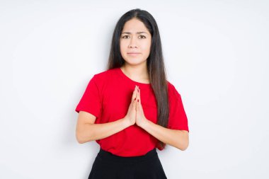 Yalvarıyor ve umut ifade yüzünde çok duygusal ve endişe ile birlikte elleriyle dua izole arka plan üzerinde kırmızı t-shirt giyen güzel esmer kadın. Bağışlanmak. Din kavramı.