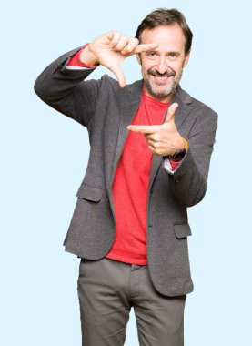 Orta yaş yakışıklı iş adamı elle yapma çerçeve ve parmakları ile mutlu yüz gülümseyerek. Yaratıcılık ve Fotoğrafçılık kavramı.