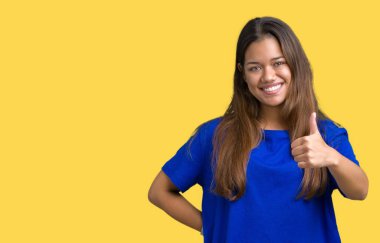 Hareketi el ile mutlu yaşasın yapıyor izole arka plan üzerinde mavi t-shirt giyen genç güzel esmer kadın. Başarı gösteren kameraya bakarak ifade onaylama.