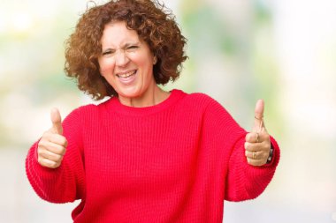 Güzel orta ager üst düzey kadın kırmızı kış kazak el ile pozitif jest yapıyor onaylama izole arka plan üzerinde başparmak gülümseyen ve başarı için mutlu. Kamera, kazanan jest arıyorsunuz.