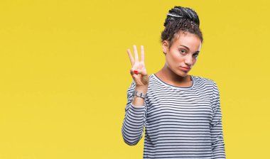 Gösterilen arka plan üzerinde kazak giyen genç örgülü saç Afro-Amerikan Kız izole ve parmakları ile işaret kendinden emin ve mutlu gülümseyerek iken üçüncü.