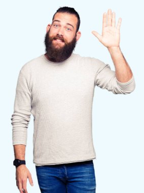 Casual kazak Waiving selam söyleyerek mutlu ve gülümseyerek giyen genç sarışın adam, dostça karşılama jest