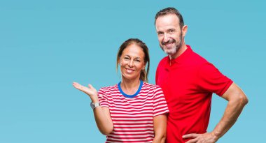 Orta yaş İspanyol çift neşeli sunulması ve kameraya bakarak avucunun ile işaret gülümseyen izole arka plan üzerinde aşık.