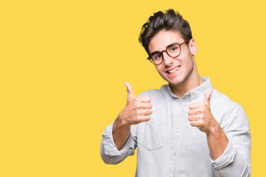 Yakışıklı delikanlı izole arka plan başarı işareti el ile pozitif jest yapıyor üzerinde gözlük takan başparmak gülümseyen ve mutlu. Neşeli bir ifadeyle, kazanan jest kameraya bakıyor.