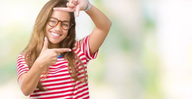 Giyen genç güzel esmer kadın gözlük ve t-shirt elle yapma çerçeve ve parmakları ile mutlu yüz gülümseyen izole arka plan üzerinde çizgili. Yaratıcılık ve Fotoğrafçılık kavramı.