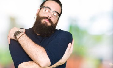 Uzun saç ve sakal kendini mutlu ve olumlu sarılma, kendinden emin gülümseyen gözlüklü genç hipster adam. Kendi aşk ve öz bakım