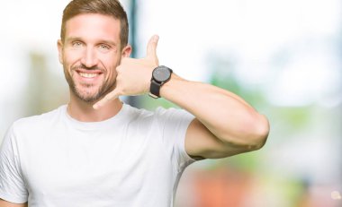Yakışıklı adam rahat beyaz t-shirt giyen gülümseyen el ve parmak telefonda konuşmak ile telefon jest yapıyor. Kavramları iletişim.