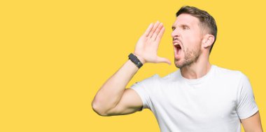 Yakışıklı adam bağırarak ve ağzı üzerinde el ile yan için çığlık casual beyaz t-shirt giyiyor. İletişim kavramı.