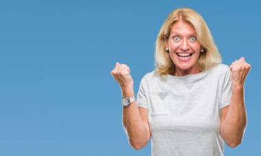 Orta yaş sarışın kadın kutluyor izole arka plan üzerinde şaşırttı ve başarı için kaldırdı kollarını açarak hayret ve gözleri açık. Kazanan kavramı.