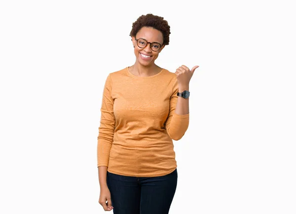 年轻美丽的非洲裔美国妇女戴眼镜在孤立的背景微笑着与快乐的脸看着和手指的一侧与拇指 — 图库照片