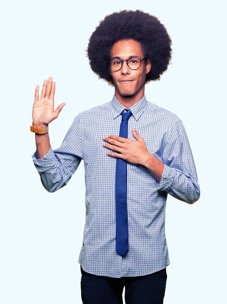 Young african american business man with afro hair wearing glasses Swearing with hand on chest and open palm, making a loyalty promise oath