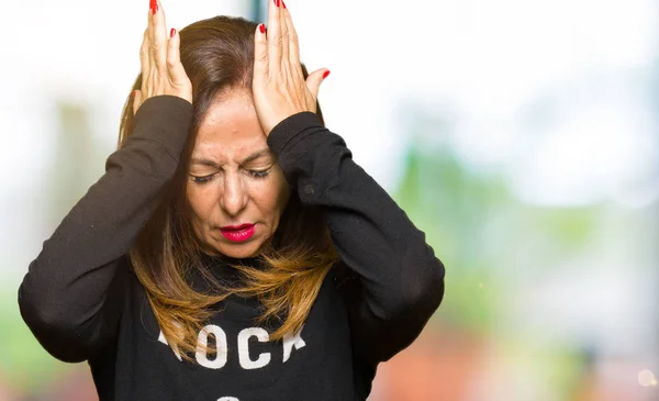 Beautiful middle age woman wearing rock and roll sweater suffering from headache desperate and stressed because pain and migraine. Hands on head.