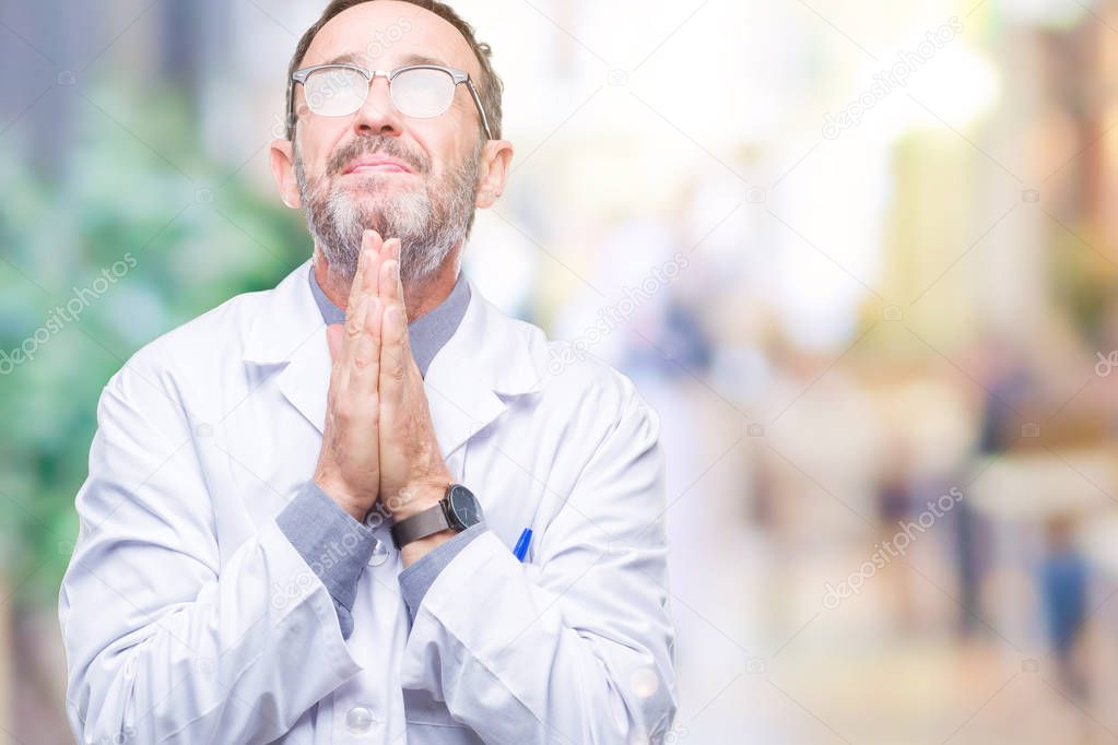 Middle age senior hoary professional man wearing white coat over isolated background praying with hands together asking for forgiveness smiling confident.