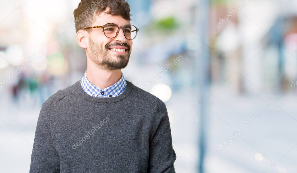 Young handsome smart man wearing glasses over isolated background looking away to side with smile on face, natural expression. Laughing confident.