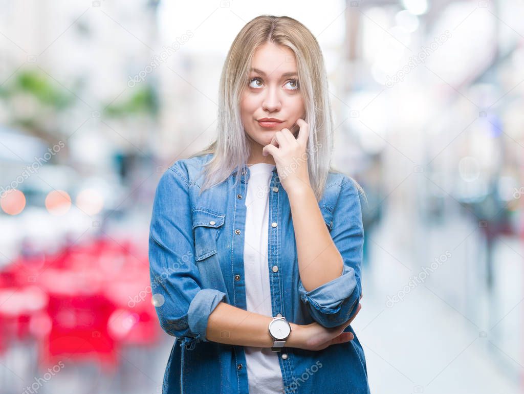 Young blonde woman over isolated background with hand on chin thinking about question, pensive expression. Smiling with thoughtful face. Doubt concept.