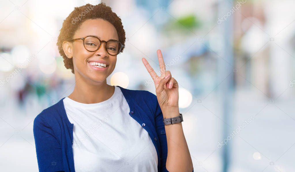 Young beautiful african american woman wearing glasses over isolated background smiling with happy face winking at the camera doing victory sign. Number two.