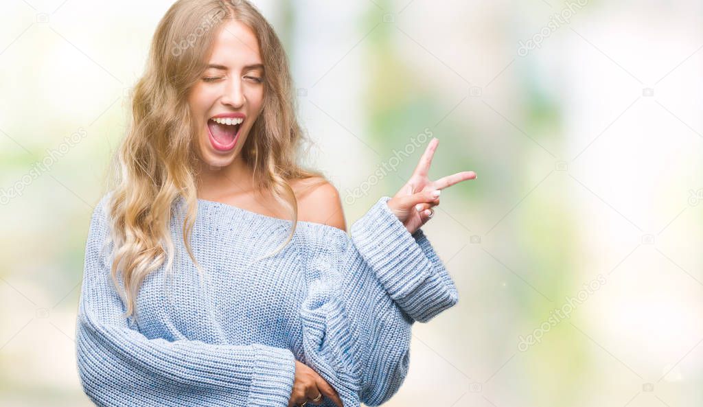 Beautiful young blonde woman wearing winter sweater over isolated background smiling with happy face winking at the camera doing victory sign. Number two.
