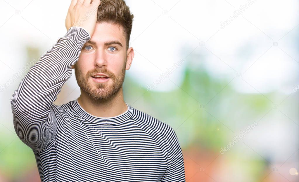 Young handsome man wearing stripes sweater surprised with hand on head for mistake, remember error. Forgot, bad memory concept.