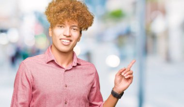 Yüzünde kocaman bir gülümseme ile afro saçlı Genç yakışıklı iş adam kameraya bakarak yan el ve parmak ile işaret.