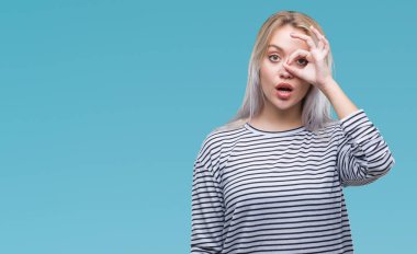 Sürpriz yüz, göz parmaklarının arasından seyir ile ok jest yapıyor izole arka plan üzerinde sarışın genç kadın şok. İmansız ifade.