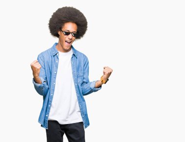 Eşkıya Hayatı'nı giyen afro saçlı genç Afro-Amerikan adam çok mutlu ve heyecanlı kaldırdı Kollarını açarak kazanan jest yapıyor, gülümseyen ve başarı için çığlık gözlük. Kutlama kavramı.