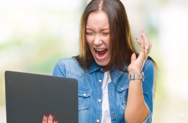 Dizüstü bilgisayar üzerinde kocaman bir gülümseme ile çığlık zaferini kutluyor ve ellerini kaldırdı izole arka plan çok mutlu ve heyecanlı, kazanan ifade kullanan genç beyaz kadın