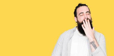 Uzun saç, sakal ve küpe sıkılmış esneme el ağzıyla kapsayan yorgun olan genç adam. Restless ve uyku hali.