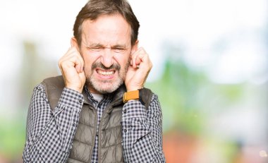 Orta yaş yakışıklı adam yüksek sesle müzik gürültü rahatsız ifade parmaklarıyla kulaklarıyla kapsayan kış yelek giyiyor. Sağır kavramı.