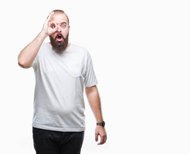 Sürpriz yüz, göz parmaklarının arasından seyir ile ok jest yapıyor izole arka plan üzerinde rahat t-shirt giyen genç beyaz hipster adam şok. İmansız ifade.