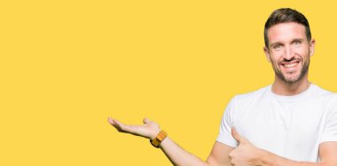 Casual beyaz t-shirt gösteren giyen yakışıklı adam palm el ve yukarıya, mutlu ve neşeli gülümseyen baş parmakları Tamam jest yapıyor