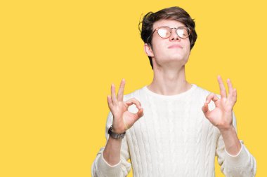 Genç yakışıklı adam gözlük izole arka plan üzerinde dinlenmek ve gülümseyen gözlerle parmak ile meditasyon jest yapıyor kapalı. Yoga kavramı.