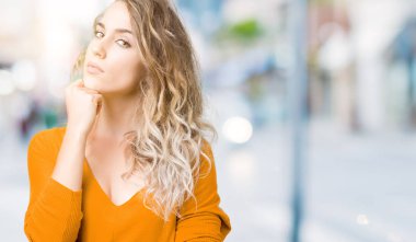 Güzel sarışın genç kadın elle çene düşünme hakkında soru, dalgın ifade izole arka plan üzerinde. Düşünceli yüzüyle gülümsüyor. Şüphe kavramı.