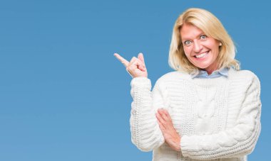 Kameraya bakarak yan el ve parmak ile işaret yüzünde kocaman bir gülümseme ile izole arka plan üzerinde kış kazak giyen orta yaş sarışın kadın.