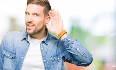 Bir işitme söylenti ya da dedikodu için dinleme kulak üzerinde el ile gülümseyen denim ceket giyen sakal ve mavi gözlü yakışıklı adam. Sağırlık kavramı.