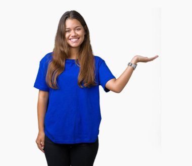 Neşeli sunulması ve kameraya bakarak avucunun ile işaret gülümseyen izole arka plan üzerinde mavi t-shirt giyen genç güzel esmer kadın.