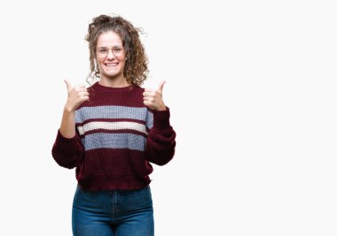 Güzel esmer kıvırcık saçlı Genç kız el ile pozitif jest yapıyor izole arka plan başarı işareti üzerinde gözlük takan başparmak gülümseyen ve mutlu. Neşeli bir ifadeyle, kazanan jest kameraya bakıyor.