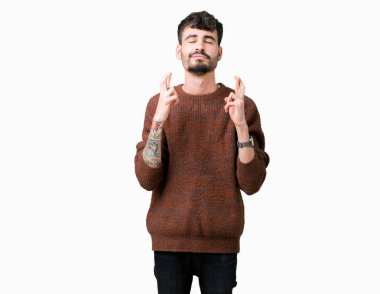 Geçiş parmakları umut ve gözleri kapalı ile gülümseyen izole arka plan üzerinde kış kazak giyen genç yakışıklı adam. Şans ve batıl kavramı.